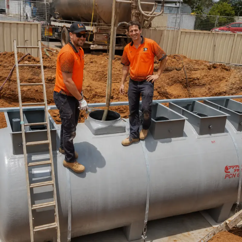 Two workers in orange hi-vis standing on a large wastewater fuji clean tank during installation